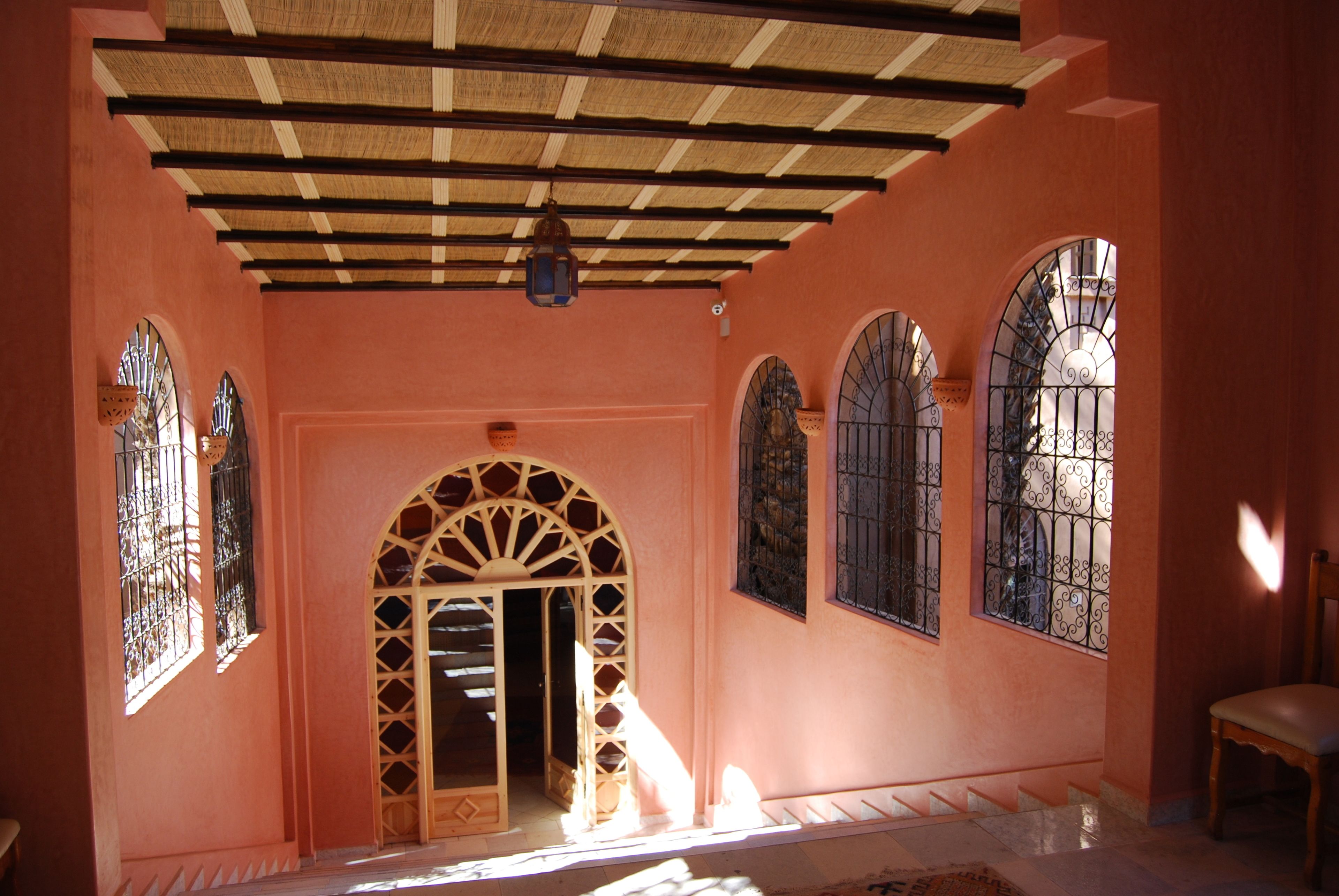 Um corredor com teto de madeira, janelas em arco com grades de metal e uma cadeira.