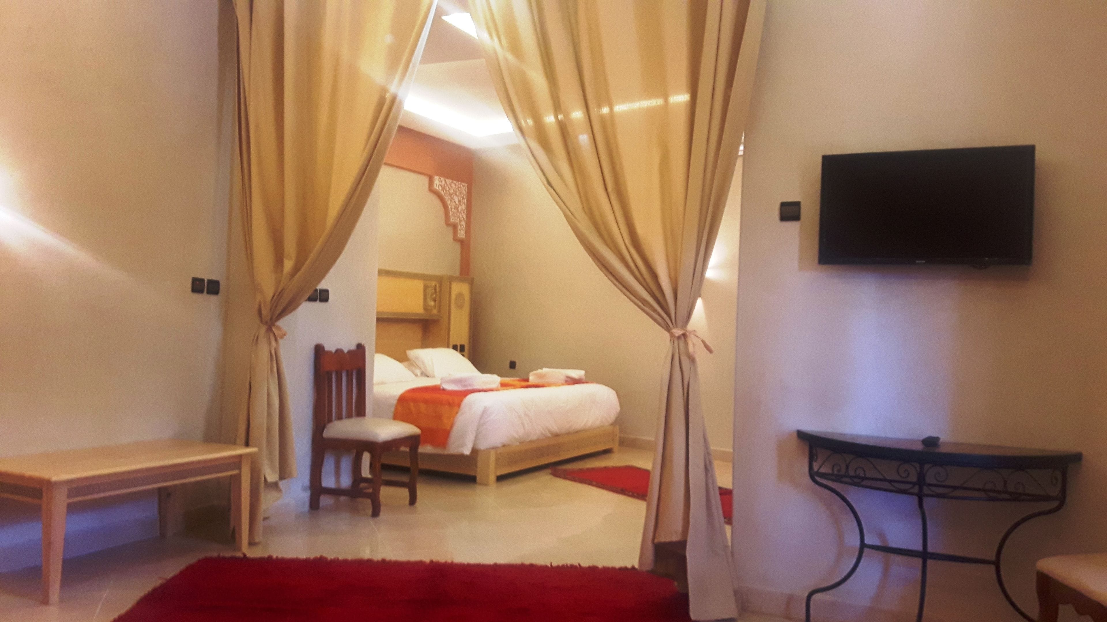 A hotel room with a bed, a chair, a small table, and a TV on the wall.