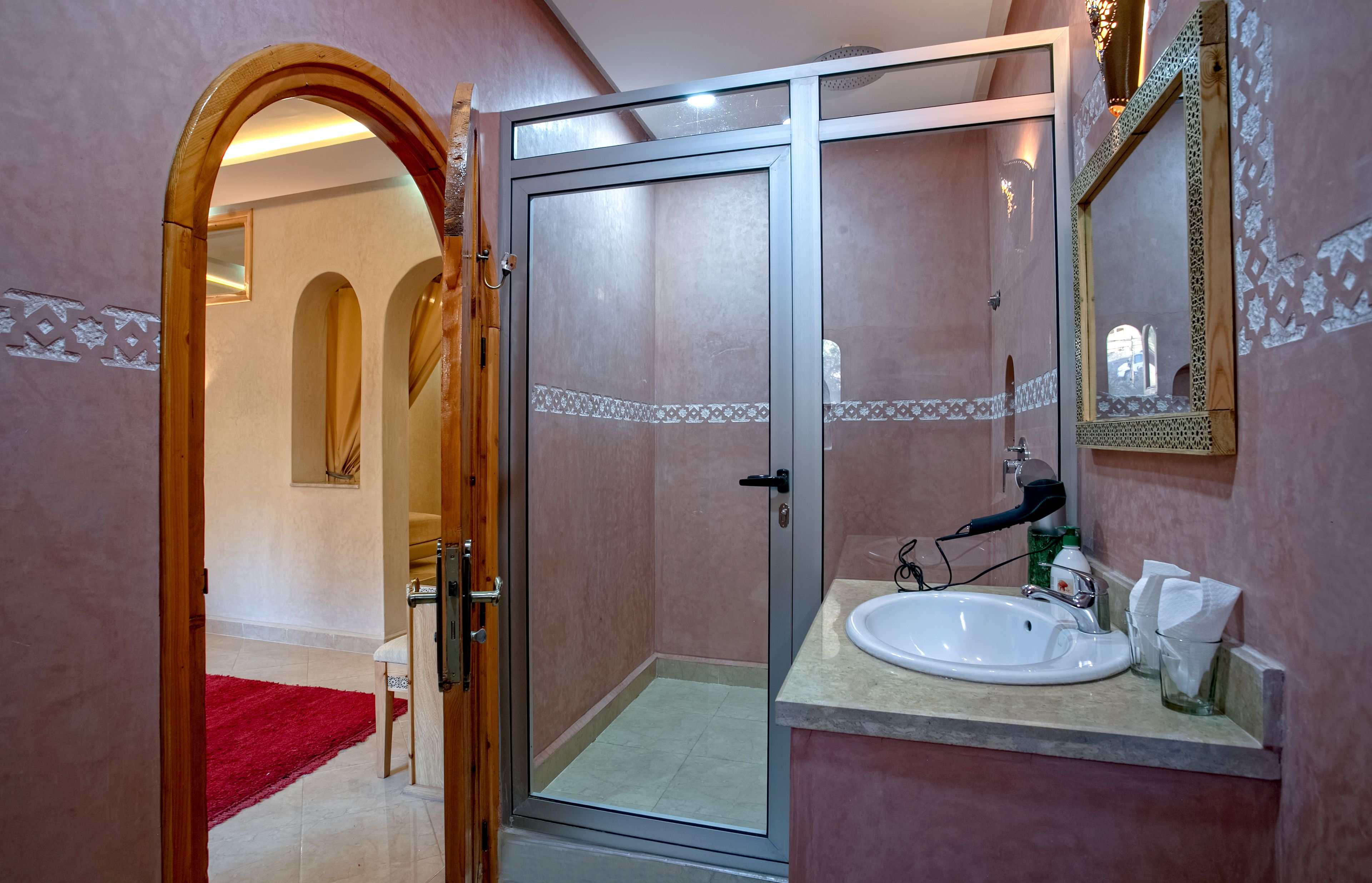 Un baño con cabina de ducha de vidrio, un lavabo con espejo y una alfombra roja que lleva a una puerta.