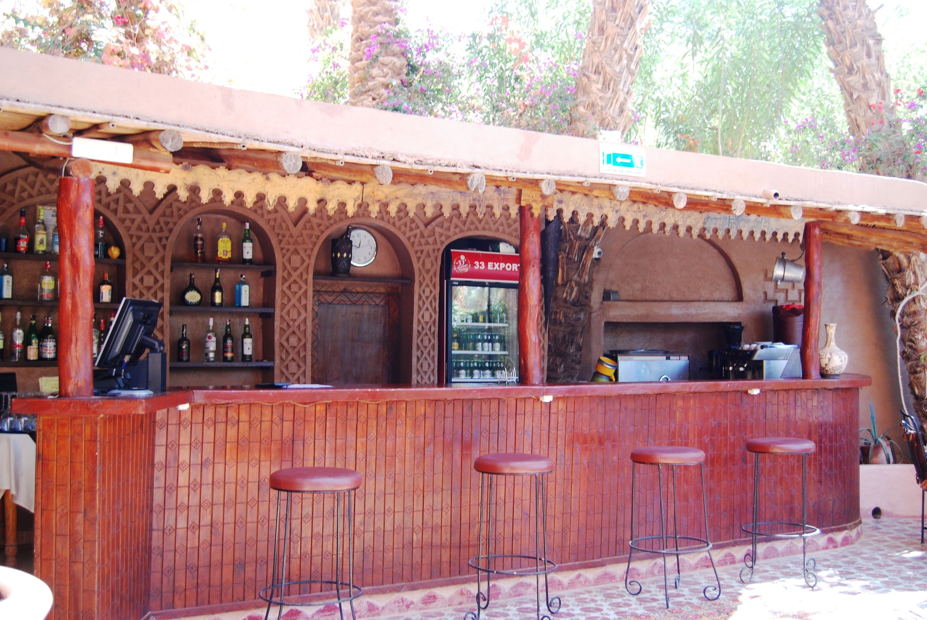 A bar with a wooden counter, bar stools, and a clock. There are shelves with bottles and a sign that says "33 Export".
