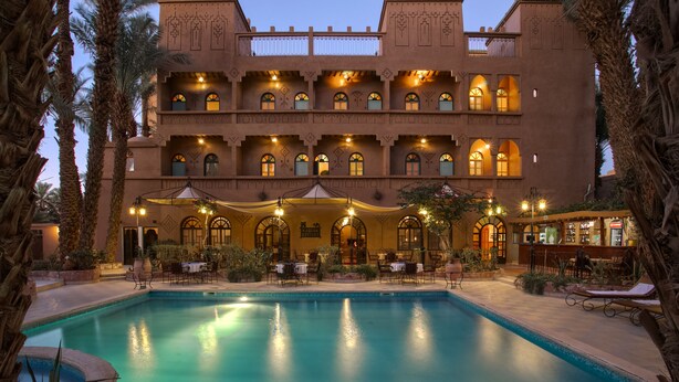 A large building with multiple balconies and arched windows, a swimming pool, and outdoor seating areas. - Kasbah Sirocco (Zagora)