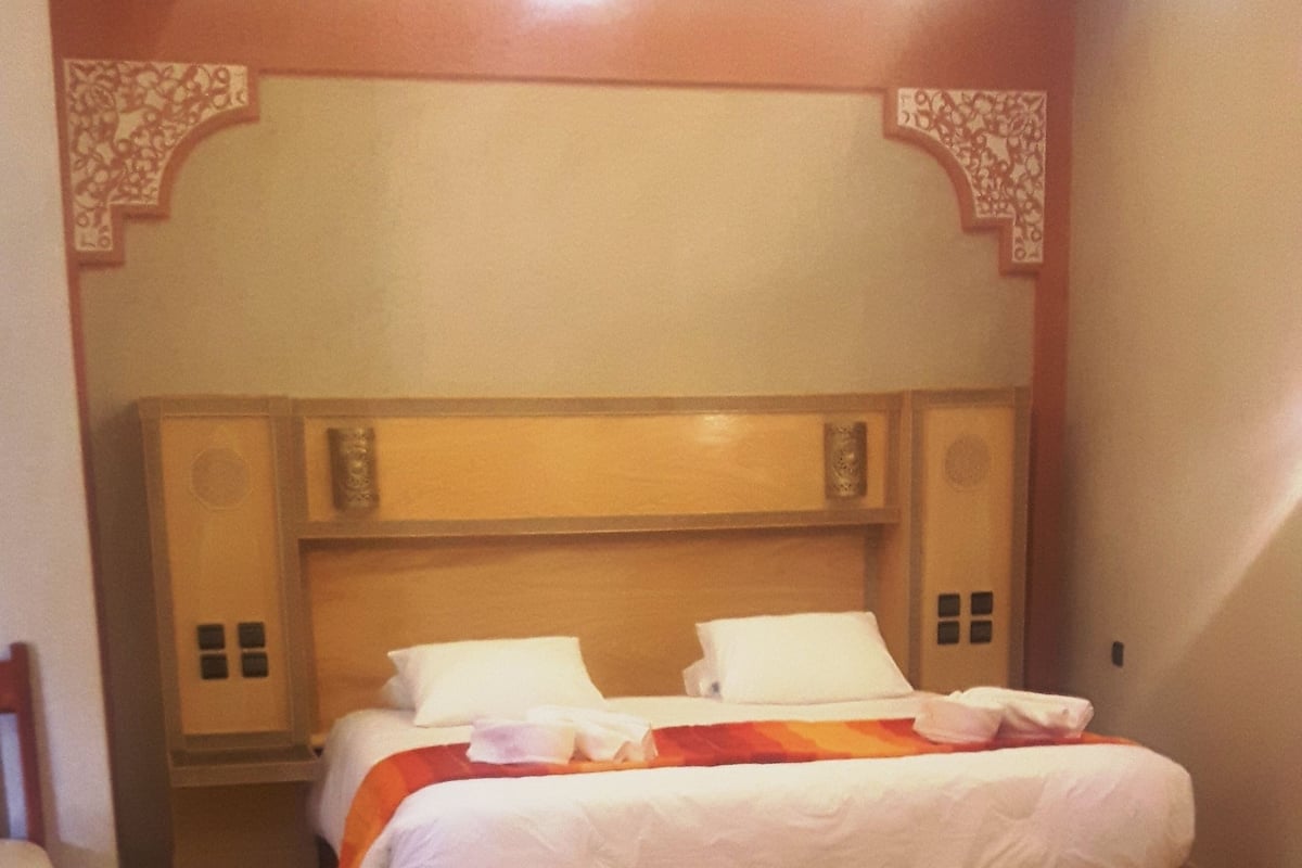 Un dormitorio con una cama grande, cabecera de madera, alfombra roja y una silla pequeña.