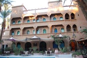 A multi-story building with balconies, arched windows, and outdoor seating areas. - Kasbah Sirocco (Zagora)