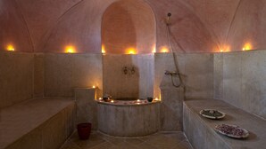 A stone-walled room with a central bathtub, candles, and a shower. - Kasbah Sirocco (Zagora)