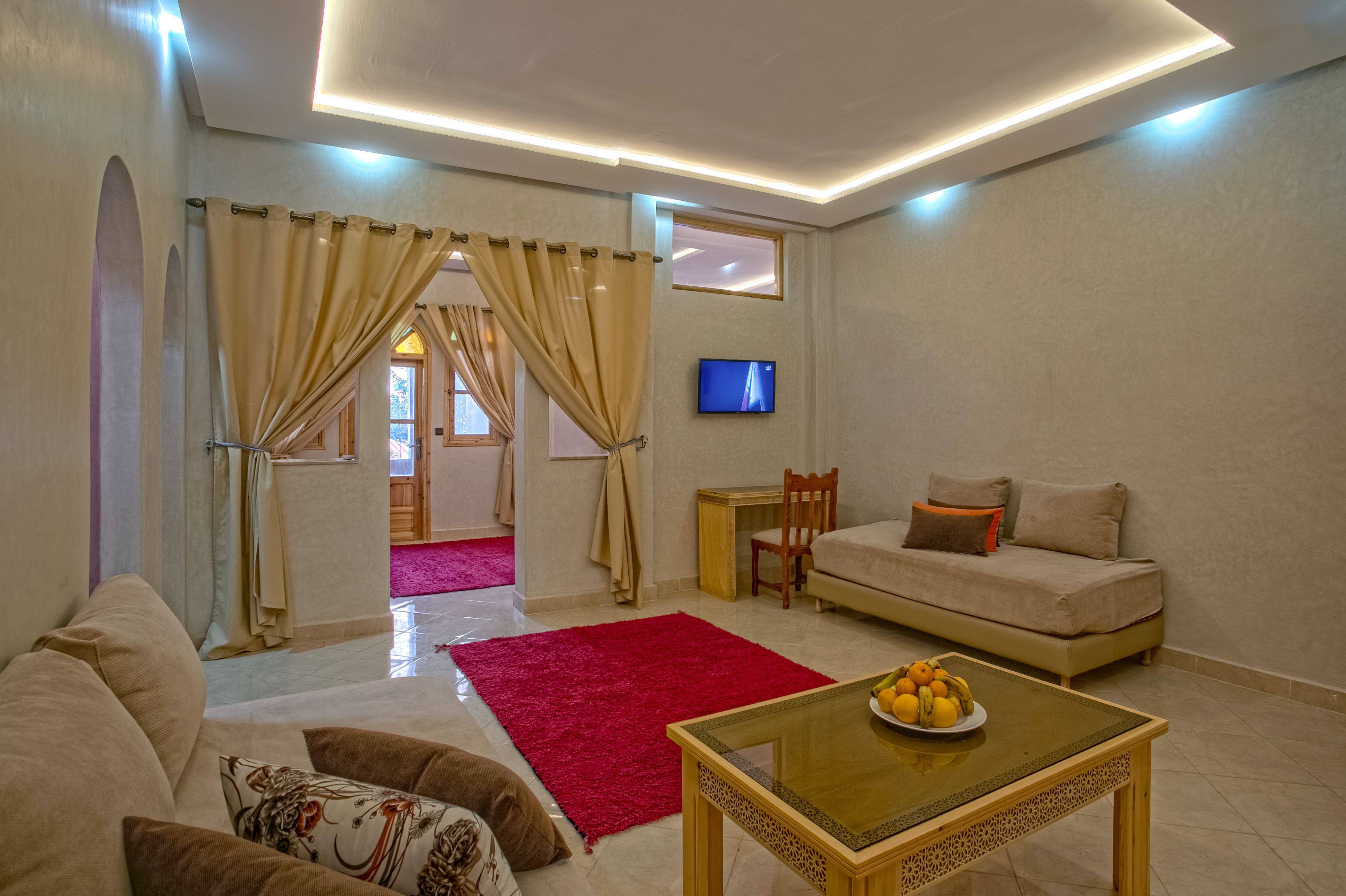 A modern living room with a sofa, a coffee table with fruit, a TV, and a red rug.