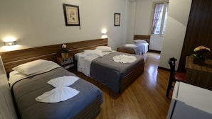 Habitación de hotel con dos camas, cabeceros de madera, mesitas de noche con lámparas, cuadros enmarcados en las paredes y suelo de madera.