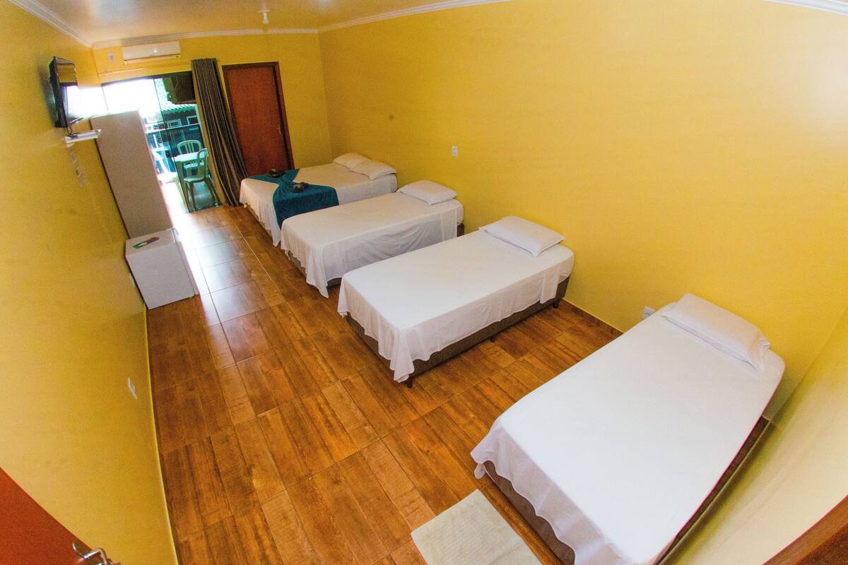 A corridor with four single beds lined up against a yellow wall, wooden flooring, and a door leading to an outdoor area.