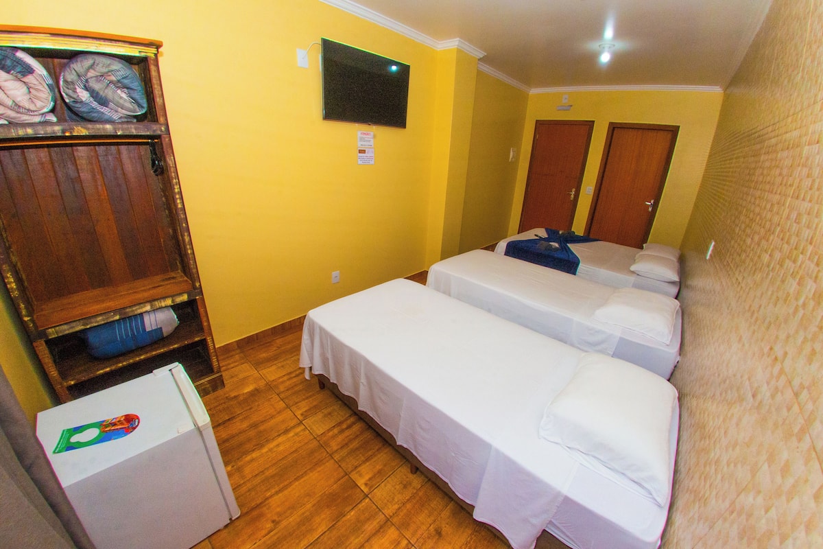 A hotel room with two single beds, a small refrigerator, a television on the wall, and a wooden cabinet.
