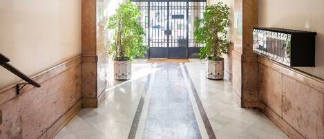 A marble-floored hallway with a black gate, potted plants, and a wall-mounted TV.