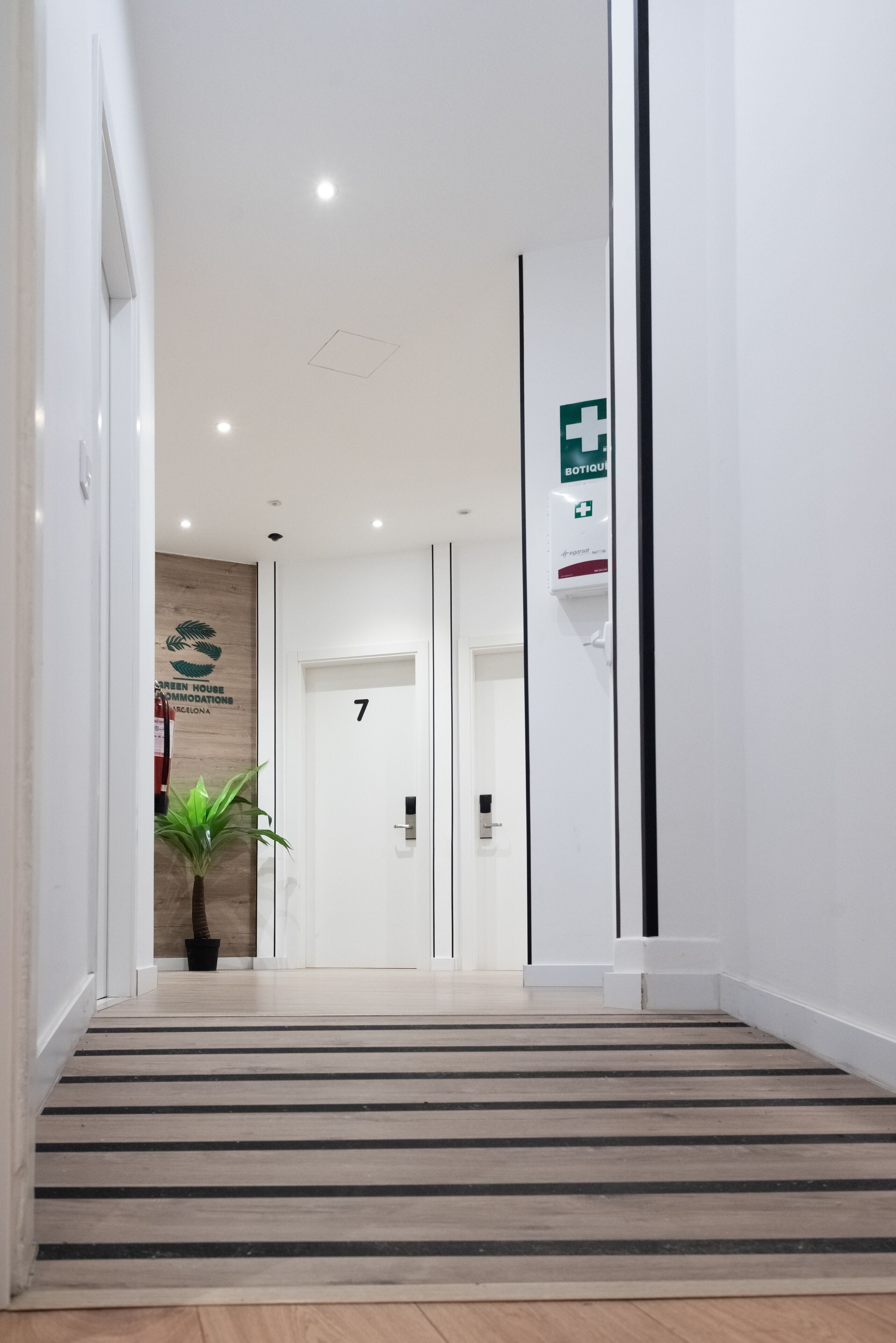 A modern hotel hallway with a wooden floor, a potted plant, and a sign indicating room number 7.