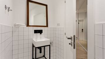 Un baño moderno con un lavamanos blanco, un espejo con marco de madera y una pared revestida de azulejos.