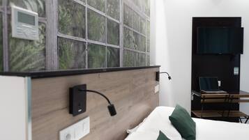 Habitación de hotel moderna con cabecera de madera, un ventanal con vistas a zonas verdes, televisor de pantalla plana en la pared y un escritorio con una computadora portátil.
