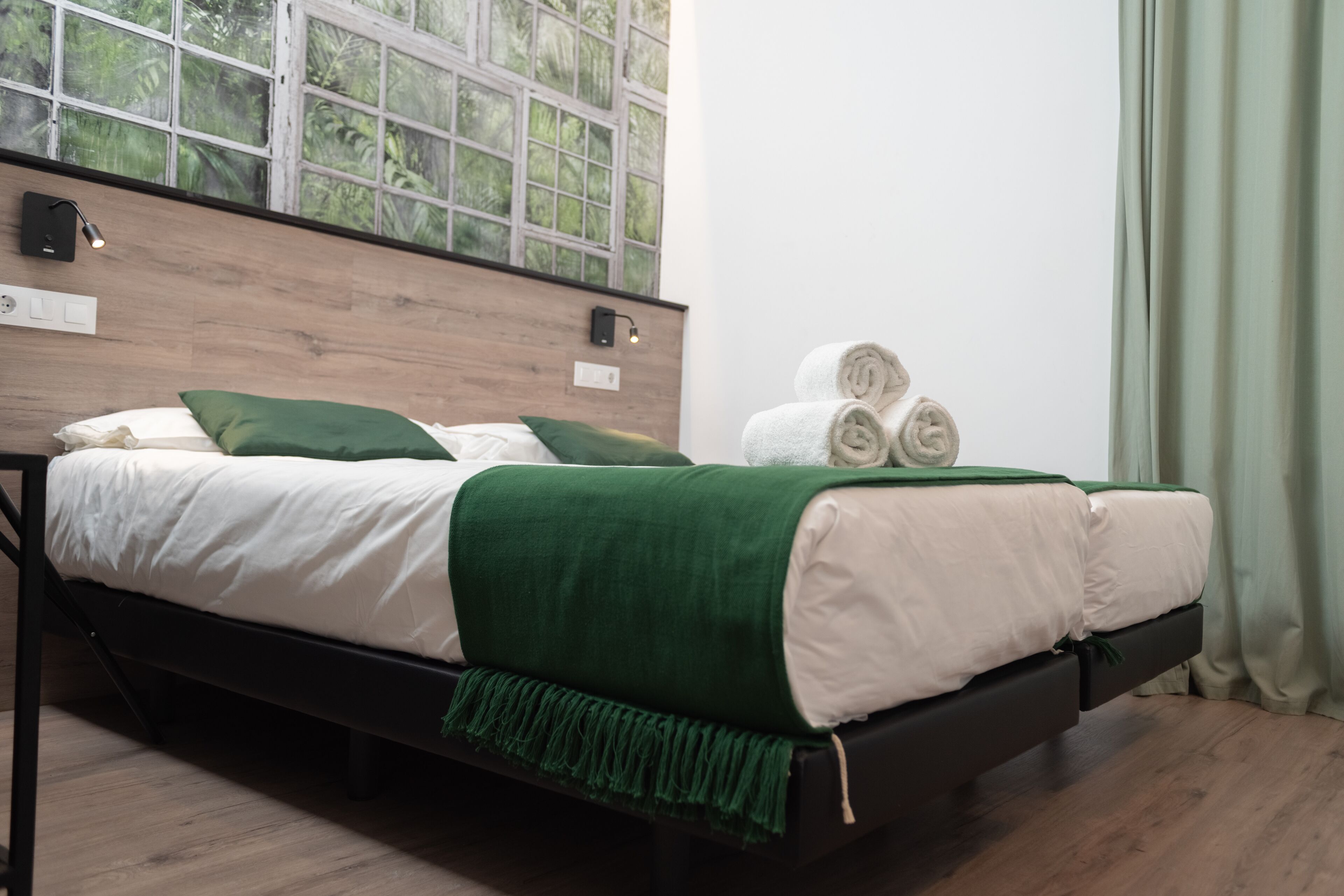 A bed with white and green bedding, a wooden headboard, and a window with a view of greenery.