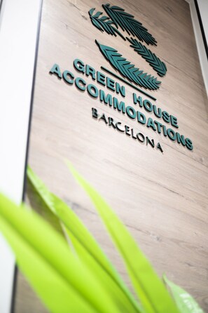 A wooden sign with the text "GREEN HOUSE ACCOMMODATIONS BARCELONA" and a logo above it.