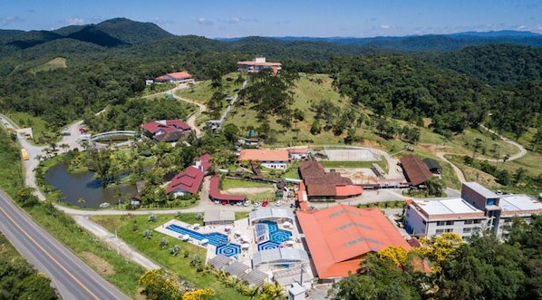 Une vue aérienne d’un complexe hôtelier comprenant plusieurs bâtiments, une piscine et une route qui longe l’ensemble.