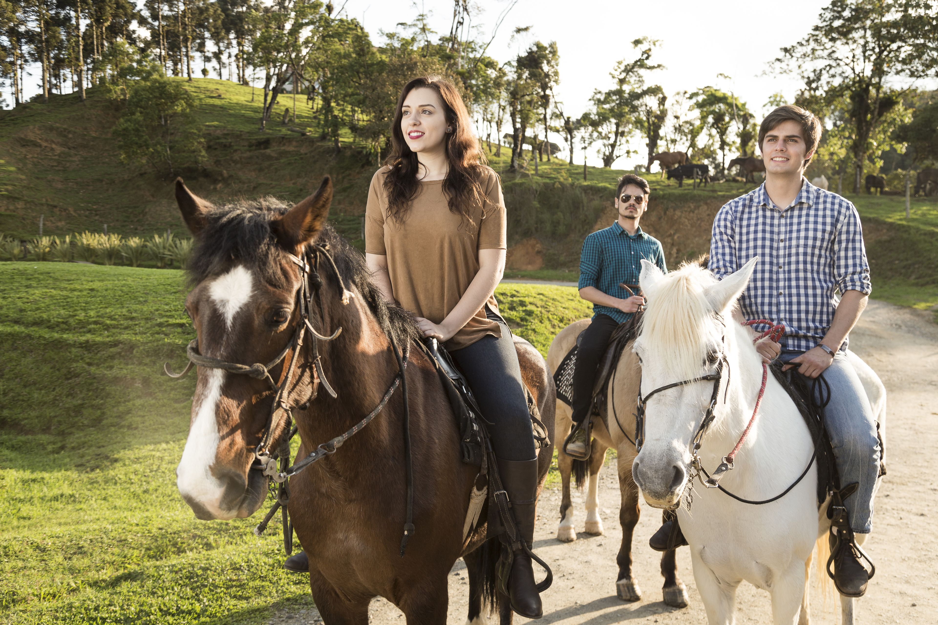 Tres personas montando a caballo por un sendero de tierra, con una colina cubierta de hierba y árboles al fondo.