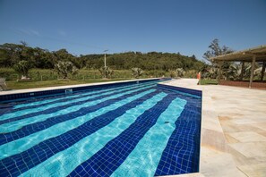 Une piscine aux carreaux bleus, entourée d’une terrasse en pierre et de verdure.