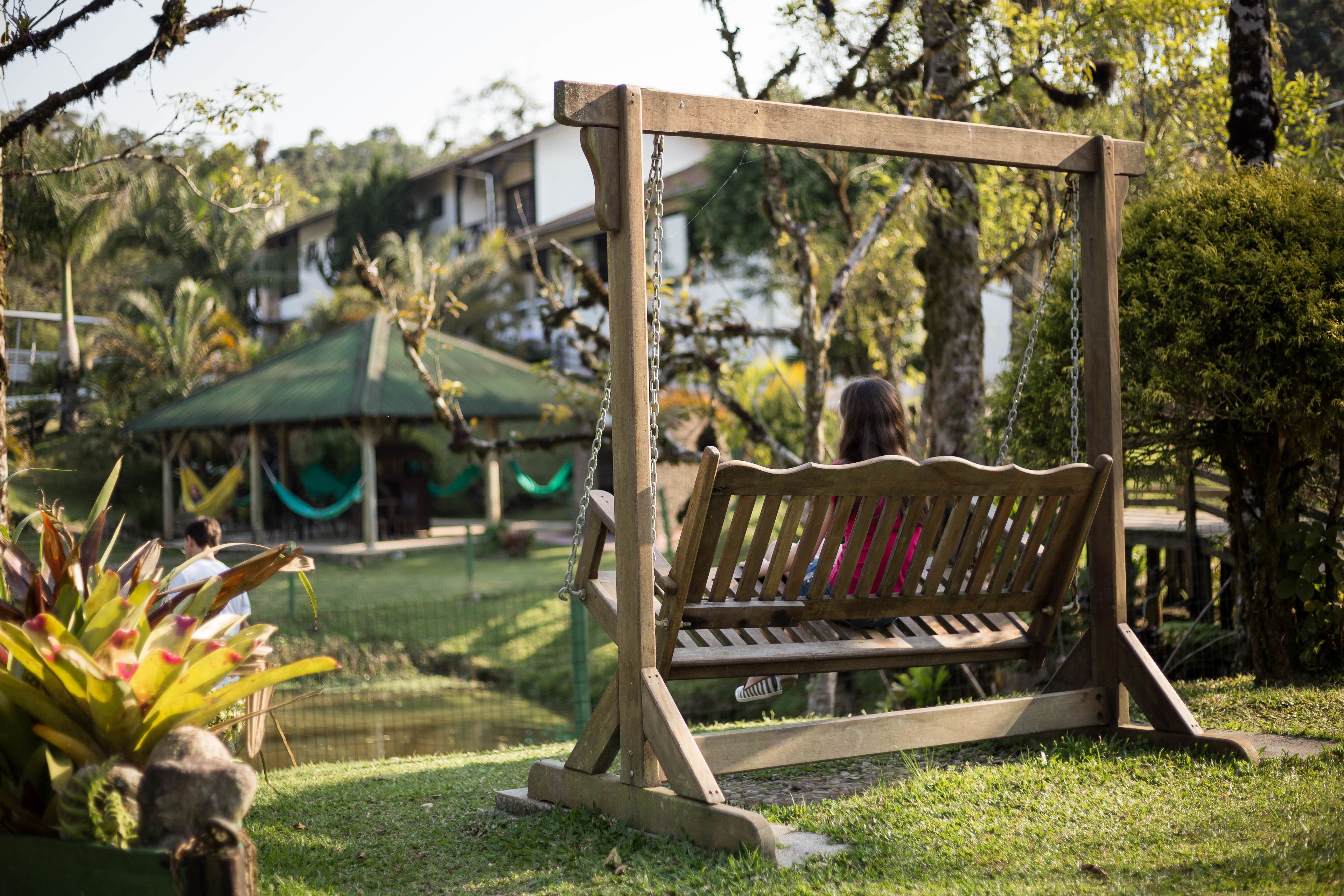 A wooden swing set in a lush garden with a hammock and a house in the background.