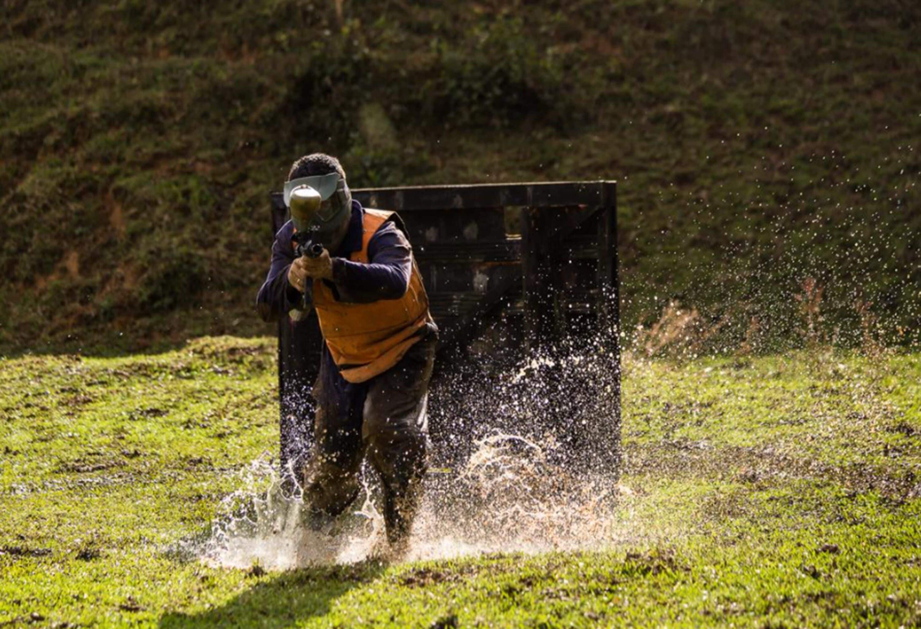 A person in protective gear spraying water in a grassy field.