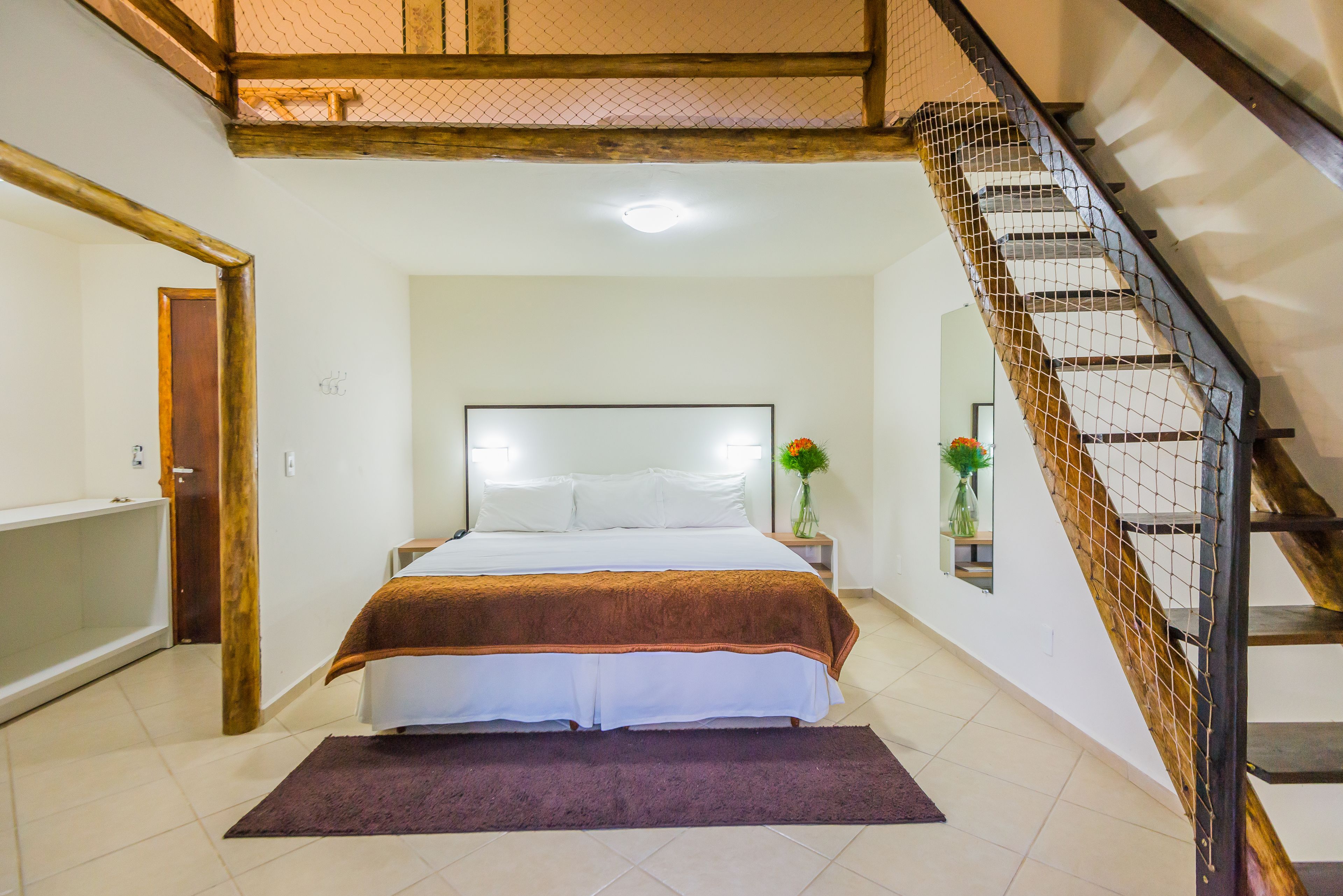 A bedroom with a bed, a nightstand, a vase with flowers, and a staircase.