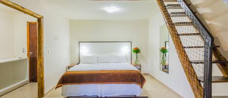 Un dormitorio con una cama, una mesita de noche, un jarrón con flores y una escalera.
