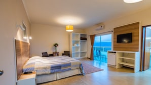 A modern bedroom with a bed, a desk, a TV, and a balcony with a view.