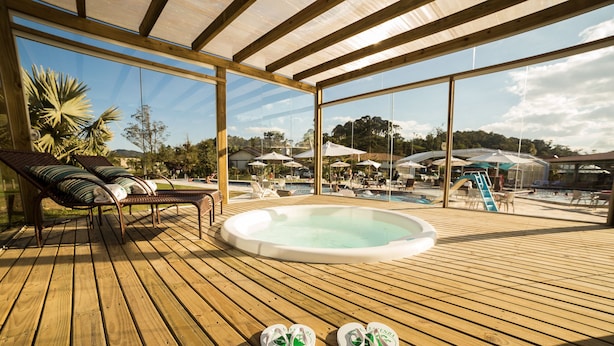A wooden deck with lounge chairs, a hot tub, and a pool area with umbrellas.