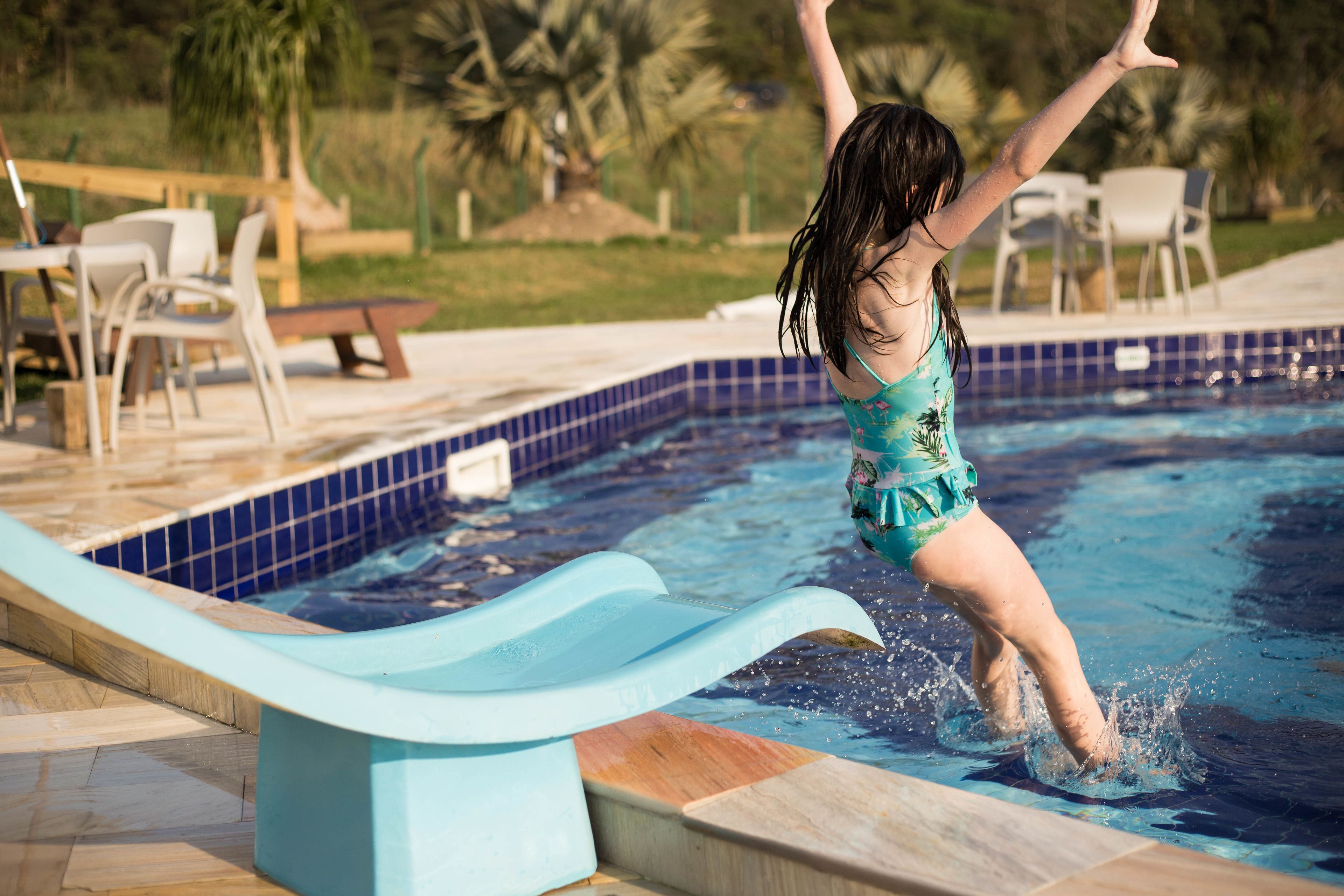 A child jumping into a pool with a slide.