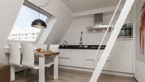 A modern kitchen with white cabinets, a wooden dining table, and a black pendant light. - Beach House Egmond aan Zee (Egmond aan Zee)