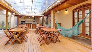 An outdoor patio with wooden tables and chairs, a hammock, and a glass ceiling. - Pousada Tissiano (Florianópolis)