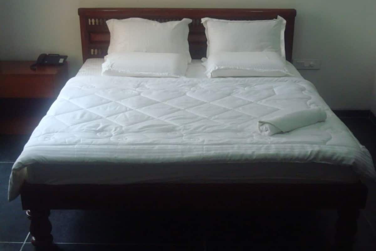 A neatly made bed with a white quilt, two pillows, and a rolled towel.