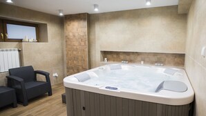 Ein modernes Badezimmer mit einer großen Badewanne, einer kleinen Sitzecke und einem Fenster mit Jalousien.