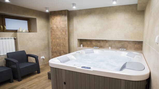 Ein modernes Badezimmer mit einer großen Badewanne, einer kleinen Sitzecke und einem Fenster mit Jalousien.