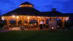 Ein Pavillon mit Lichterketten, Gartenmöbeln und einem Kamin aus Stein.