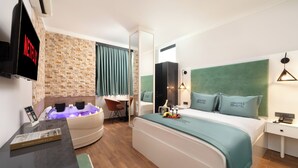 A modern hotel room with a stone wall, a large bed with green bedding, a massage chair, a TV, and a minibar. - Bakırköy DES Suit Otel (Istanbul)