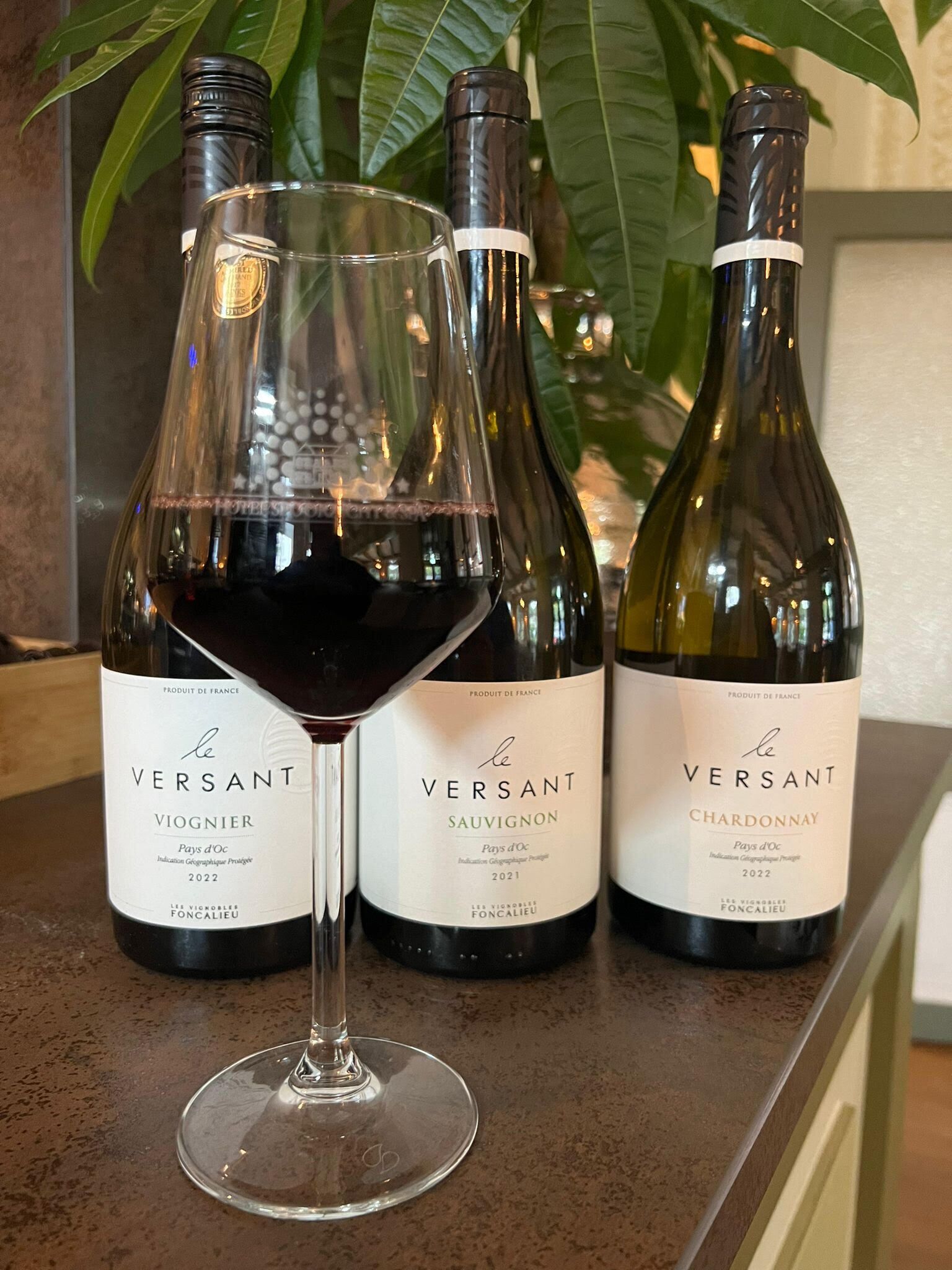 Drie flessen le Versant wijn op een aanrecht, waarvan één in een glas is geschonken.