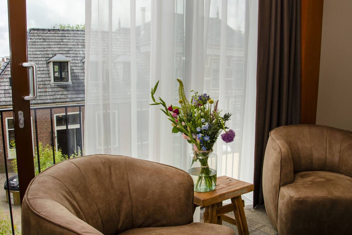 A room with a large window, a brown leather chair, a small wooden table, and a vase of flowers.
