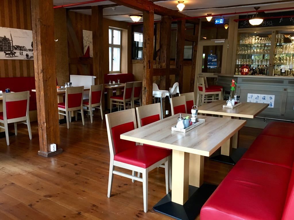 A restaurant interior with wooden floors, red cushioned booths, and a bar area with glassware.