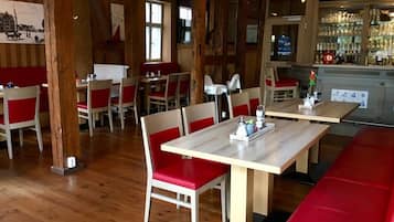 A restaurant interior with wooden floors, red cushioned booths, and a bar area with glassware.