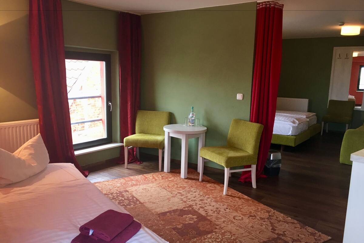 A hotel room with a bed, two chairs, a small table, and a window with curtains.