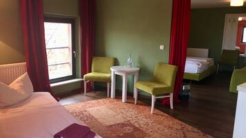 Una habitación de hotel con una cama, dos sillas, una mesita y un ventanal con cortinas.