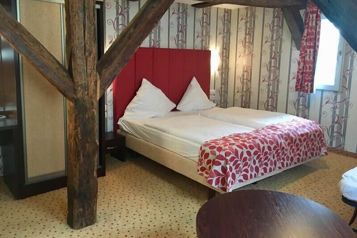 A bedroom with a wooden ceiling, a red headboard, a bed with white bedding, and a patterned throw.