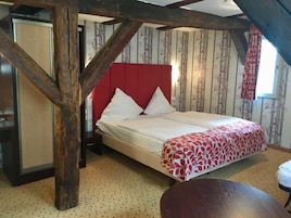 Un dormitorio con techo de madera, cabecera roja, cama con ropa de cama blanca y manta estampada.