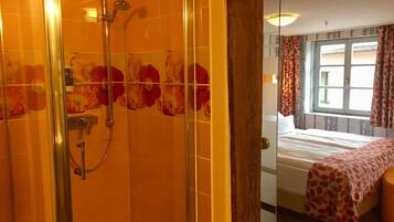 Hotellihuone, jossa on suihku, sänky ja ikkuna, jossa on verhot.
