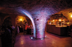 Un interior con arcos de piedra, una zona de bar y mesas con clientes.