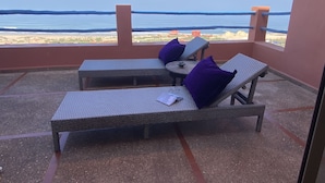 A balcony with two wicker lounge chairs, a small round table, and a view of the sea. - Daribis (Sidi Ouassay)