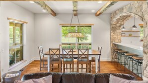 A dining area with a wooden table and chairs, a stone wall, and a kitchen area with bar stools.