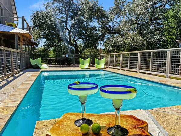 A swimming pool with two drinks on a wooden board.