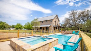 A pool area with stone walls and blue chairs, a wooden deck, and a large building in the background.