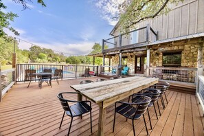 An outdoor deck with a wooden table and chairs, a pool, and a stone building with a balcony.
